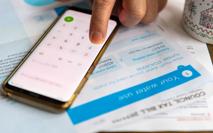 A water bill on a table, with a person's hand using a smartphone's calculator app